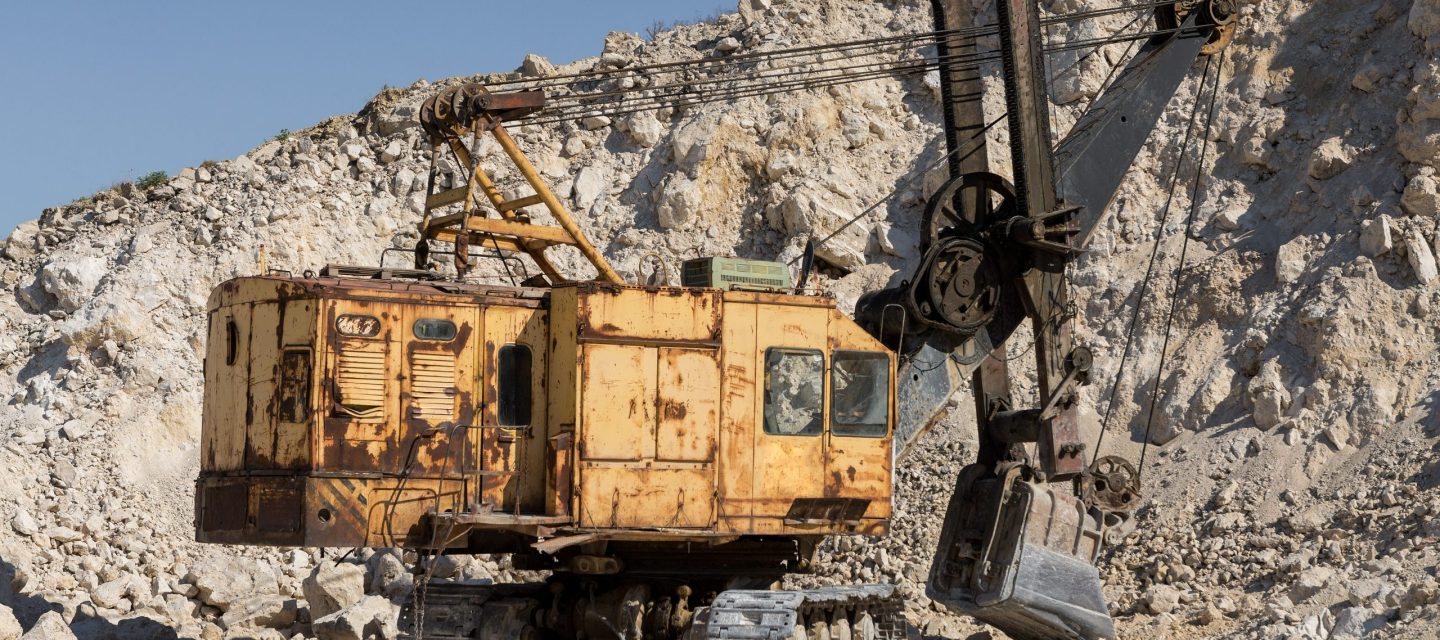 A large yellow tracked excavator is mining rock in a quarry.